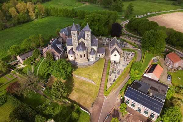 Aerial view of the Basilica of Sint Odiliënberg, a historic church building surrounded by greenery, with a cemetery and some surrounding buildings.