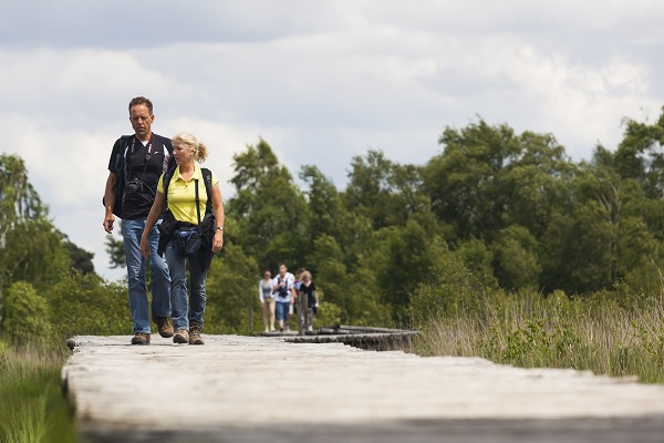 Stel wandelt over een knuppelbrug in Nationaal Park De Groote Peel