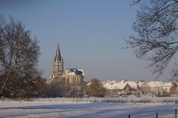 Winterse blik op de abdijkerk van Thorn, met besneeuwde daken en een wit landschap op de voorgrond.