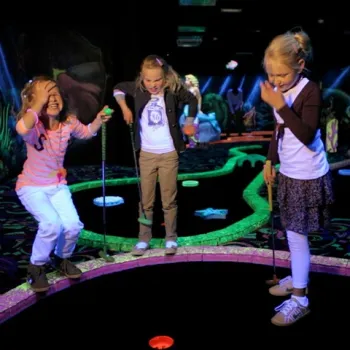 Drie jonge kinderen spelen glow in the dark minigolf in een kleurrijke indooromgeving in Limburg.