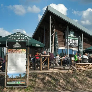 Gasten genieten van een lunch op het terras van Brasserie De Boshut bij Nationaal Park De Meinweg, met uitzicht op de natuur en een ontspannen sfeer.